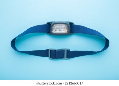 Led Headlamp With Elastic Strap On Light Blue Table Background. Pastel Color. Closeup. Equipment For Work Or Sport Activities In Dark Time.