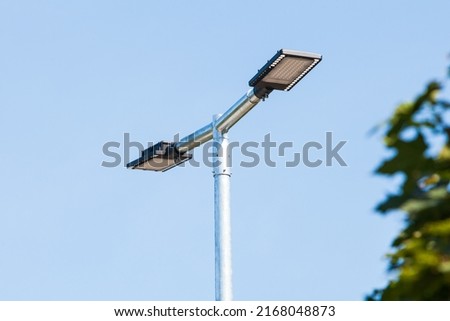 LED lantern for street lighting. modern street lamp on a metal pole next to a green tree against the blue sky in bright sunny weather. modern LED lamp street lighting