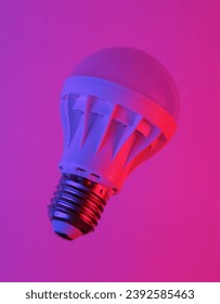 Led light bulb floating in the air, isolated in blue-red neon gradient light. Levitating objects. Creative idea. Minimal concept