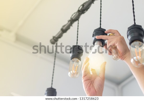 LED light Power saving\
concept. Asia man changing compact-fluorescent (CFL) bulbs with new\
 bulb.