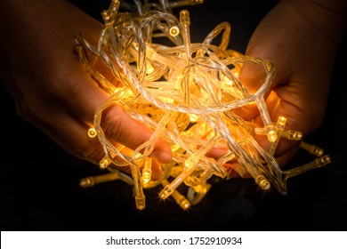 Led string lights on a black background and being held by hands. Colour Yellow. Christmas Lights,