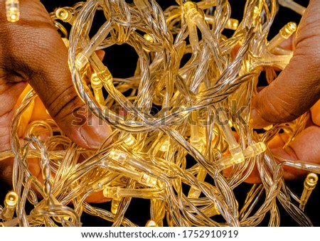 Led string lights on a black background and being held by hands. Colour Yellow. Christmas Lights,