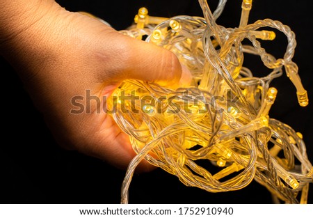 Led string lights on a black background and being held by hands. Colour Yellow. Christmas Lights,