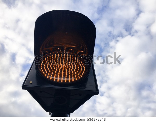LED traffic light ,orange blink on the road\
with cloud sky is\
background.