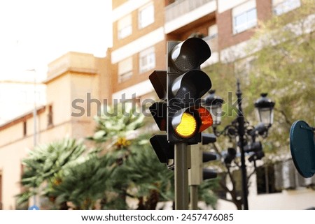 LED yellow traffic light on defocused european buildings and palms trees background. Attention. City crossing with amber light in semaphore, traffic control and regulation concept. Valencia, Spain.