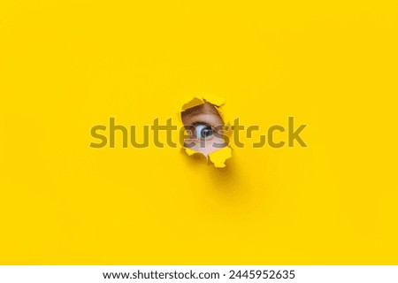The left eye looks into a hole in the yellow paper. Voyeurism. The child watches his parents. A curious look. Jealousy, voyeurism or eavesdropping concept. Copy space. Stock fotó © 