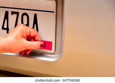 Left female hand applying annual registration year sticker with thumb pressing the sticker into place for final application on a generic license plate with copy space. 