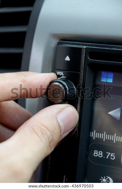 Left hand adjusting a volume control knob of the\
car\'s audio system.