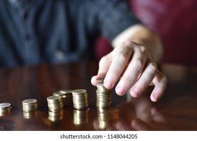 Left hand of caucasian man stacking coins into piles of different height.
 Shallow DOF

Conceptual for savings, accrual of interests, finance, investments.
