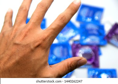 The Left Hand Of The Dark Skin That Is Reaching Out, Picks Up Many Condoms That Are Placed On The White Floor. Conveying The Choice Of Using Condoms According To Different Sizes And Models.