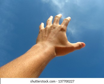 left hand extended towards the blue sky  in attempt to reach the clouds