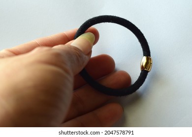 Left Hand Holding A Black Hair Tie Bracelet On A White Background