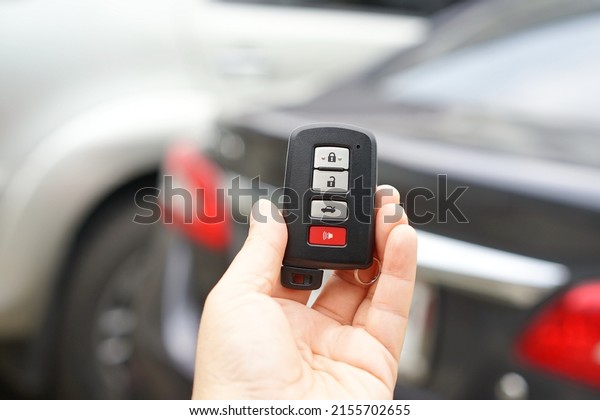 Left hand holding a black remote car key. There is\
a small ring hanging on it and three gray buttons for locking and\
unlocking the car. red button for emergency Smart key systems for\
modern cars\
