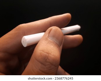 left hand holding a cigarette on an isolated black background. - Shutterstock ID 2368776245