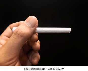 left hand holding a cigarette on an isolated black background. - Shutterstock ID 2368776249