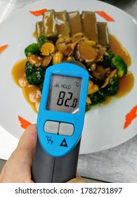 Left Hand Holding Infrared Thermometer Measuring Food Temperature. Hot Food. Food Safety First. 