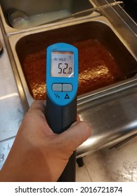 Left Hand Holding Infrared Thermometer Measuring Food Temperature. Hot Food. Food Safety First. 