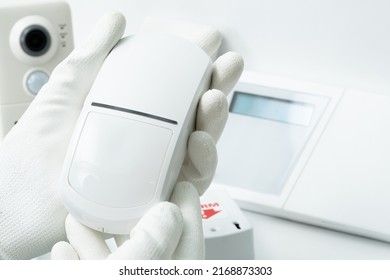 The left hand of a man in a white glove holds a motion sensor of security systems.
