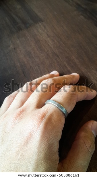 Left hand with a ring in the index finger place on\
wooden table