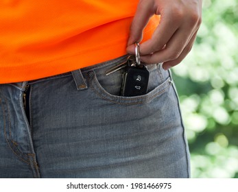Left hand taking car remote key out of gray jeans front pocket 