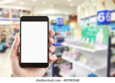 Left Hand Using Smartphone With Blank Screen On Abstract Blur Background Inside Pharmacy Store With Shelves Of Pharmaceutical And Drug.