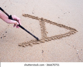 A left hand is writing A on sand