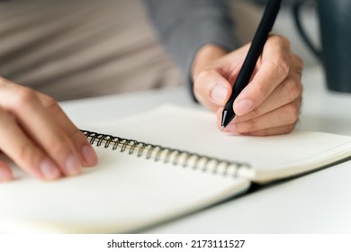 left handed man writes in a notebook on the table - Shutterstock ID 2173111527