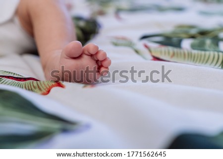 Left infant foot with small toes spread open facing the camera on a blanket on the bed