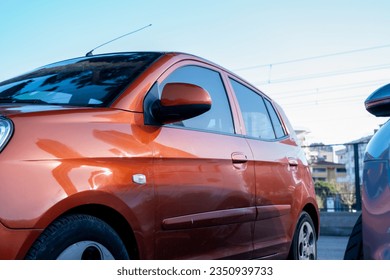 left side of an orange shining small sport car with mirror and doors in the parking lot with copy space