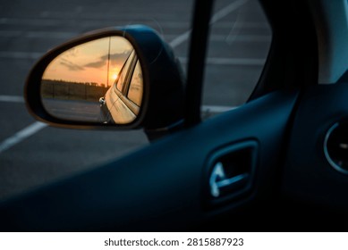 Left side rearview mirror inside a car. Close-up view of the vehicle's exterior left mirror and interior driver side panel during sunset.