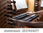 Left side view of organist playing the organ and changing the organ registers with his left hand in the Catholic Church.