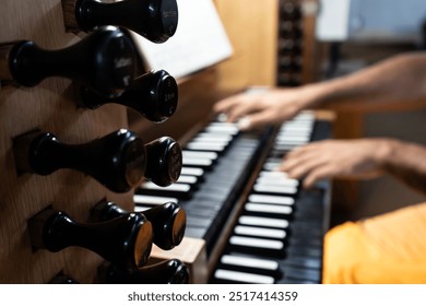 Left side view of out of focus organist's hands playing the organ in a Catholic church, focus is on the organ registers.
