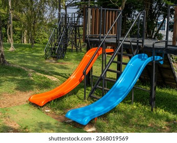 A left side view of two children slides, red and blue, and climbers on a jungle gym platform. - Powered by Shutterstock