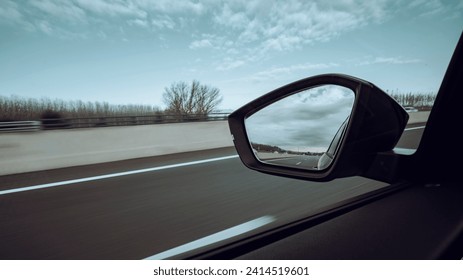 Left side window view scene of a road car on a highway on a beautiful forest landscape with sharp backward mirror