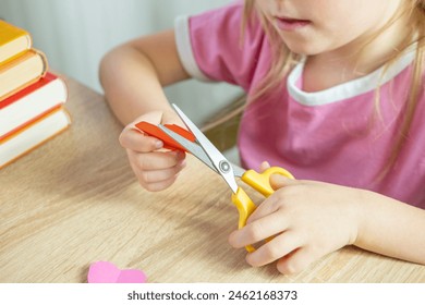 left-handed little girl learning to cut paper with scissors, making shapes like a house, heart and flowers for applique crafts