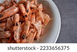 Leftover boiled shrimp in a white plate on grey background. Waste food shrimp peeled, detail of the heads and eyes of this seafood. Peeled skin and head for making a delicious broth shrimp.