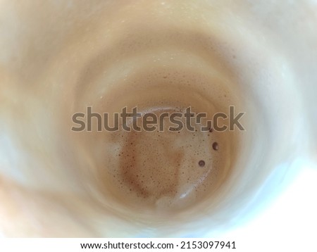 Leftover foamy cappuccino at the bottom of the white paper cup. Top view