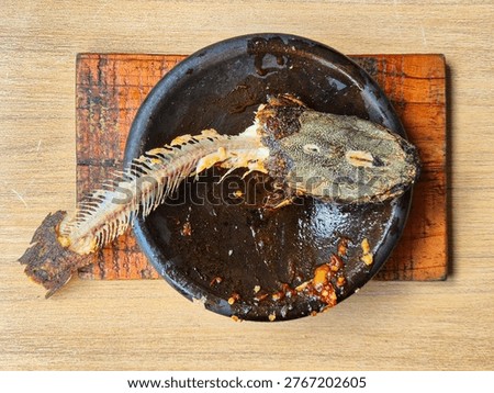 Leftover fried catfish bones and head with spicy sambal on a traditional clay plate. Perfect for food waste or culinary concepts.