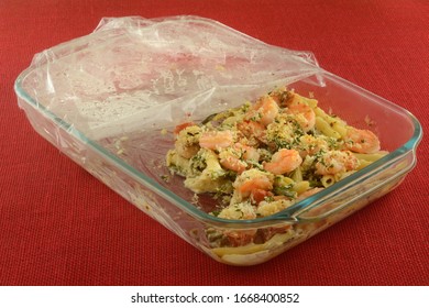 Leftovers Of Shrimp, Pasta, Tomato And Asparagus Casserole In Glass Baking Pan With Plastic Wrap Cover