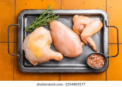 a leg, a breast, and a wing. A sprig of rosemary is placed on top of the chicken pieces. A small metal bowl filled with pink Himalayan salt sits beside the chicken. - Powered by Shutterstock