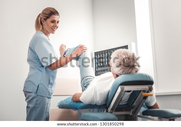 Leg exercises.\
Beautiful professional doctor doing leg exercises for man lying on\
bed after car accident