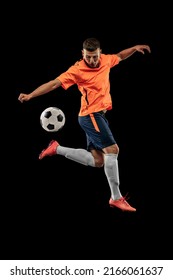 Patada de pierna. Retrato de futbolista masculino profesional en movimiento aislado en un fondo oscuro. Concepto de deporte, objetivos, competencia, hobby y. Deportistas con equipo de fútbol naranja-azul