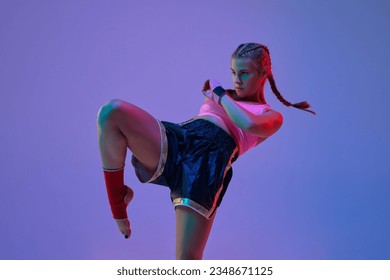 Leg kick. Sportive teen girl, mma fighter athlete in motion, training, fighting against purple background in neon lights. Concept of mixed martial arts, sport, hobby, competition, strength, ad