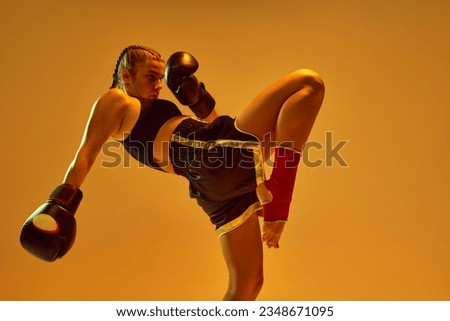 Leg kick. Sportive teen girl, mma fighter athlete in motion, training, fighting against orange studio background in neon lights. Concept of mixed martial arts, sport, hobby, competition, strength, ad
