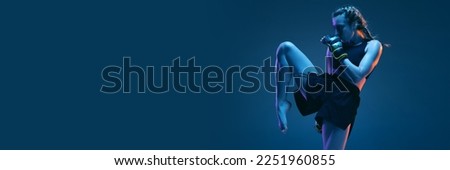 Leg kick. Young woman athletic female MMA fighter training isolated on gradient blue-pink background in neon light. Concept of sport, competition, action, healthy lifestyle. Copy space for ad.