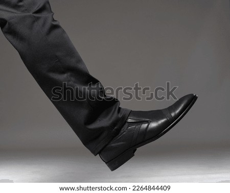 Leg of a man in elegant black trousers and leather shoes isolated on gray