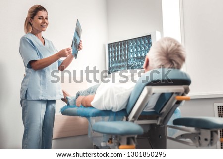 Leg roentgen. Skillful appealing chiropractor wearing blue uniform doing leg roentgen for retired man
