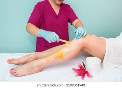 Leg Sugaring. A Beautician Makes A Sugar Paste Depilation Of A Woman's Legs In A Beauty Salon. Female Aesthetic Cosmetology. Apply Sugar Paste With A Wooden Spatula.