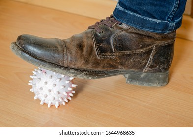 The leg of a young guy in a brown coded boot stepped on a small ball. A light rubber ball with spikes is pressed to the wooden floor with a dirty boot. Close-up. Selective focus.