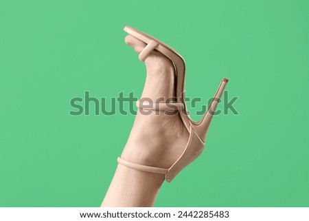 Leg of young woman in stylish beige high heel on green background